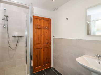 A bathroom with a shower, wooden door, wall-mounted sink, and a mirror at Speedwell in Charlestown