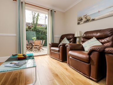 A living room with leather armchairs and a glass coffee table near a patio door opening to a garden with outdoor wooden furniture at Speedwell in Charlestown