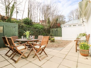 A patio with a round wooden table and chairs with cushions a bench and potted plants at Speedwell in Charlestown