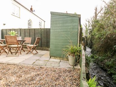 A backyard with wooden chairs and table on paving stones next to a green shed and a narrow stream at Speedwell in Charlestown