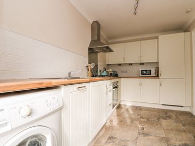 A kitchen with white cabinets wooden countertop washing machine oven microwave and tiled floor at Speedwell in Charlestown