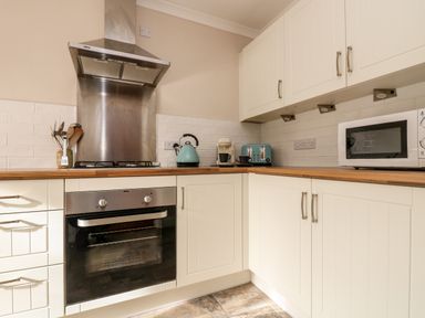 A kitchen with white cabinets a wooden countertop a gas stove an oven a kettle a coffee machine a toaster and a microwave at Speedwell in Charlestown