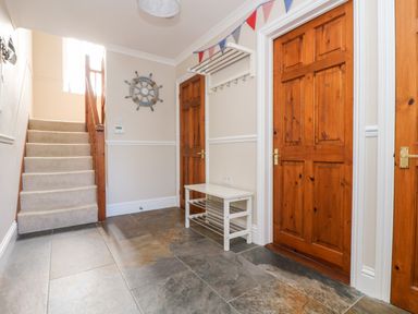 A hallway with a staircase carpeted in beige a white bench with shoe racks a wall-mounted coat rack and three wooden doors at Speedwell in Charlestown