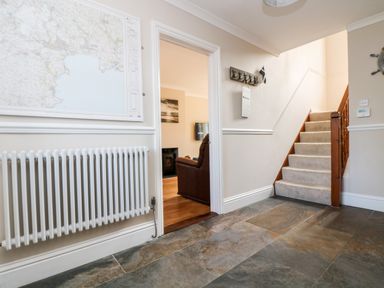 An entryway with a staircase carpeted with beige and a doorway leading to a living room with a brown armchair and wooden floor at Speedwell in Charlestown