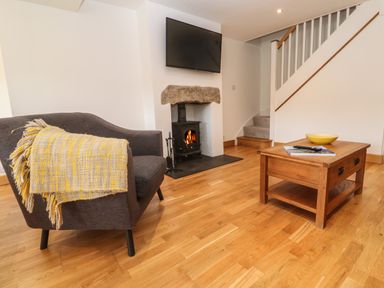 A living room with a gray armchair with a yellow blanket a wooden coffee table a fireplace under a mounted TV and stairs in the background at Anneth Lowen in Angarrack near Hayle
