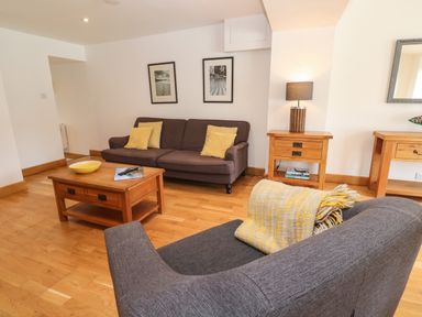 A living room with a brown sofa and yellow cushions a wooden coffee table and side tables with a lamp at Anneth Lowen in Angarrack near Hayle