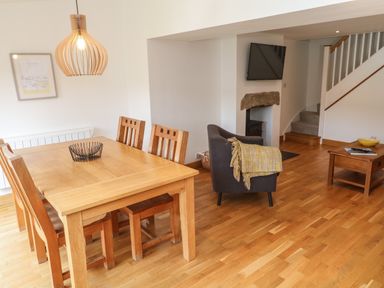 A dining area with a wooden table and chairs next to a sitting area with an armchair and a wall-mounted TV at Anneth Lowen Angarrack near Hayle