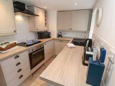 A kitchen with beige cabinets a microwave a stove oven a sink a toaster a knife block and a basket on the counter at Anneth Lowen Angarrack near Hayle