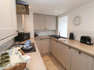 A kitchen with beige cabinets a black microwave kettle and toaster and a wicker basket on the counter at Anneth Lowen in Angarrack near Hayle