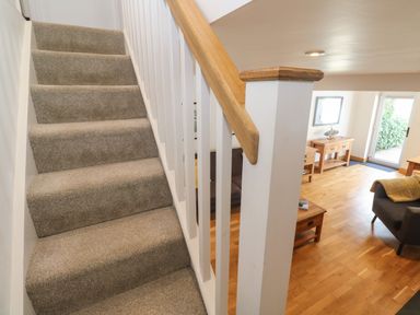 A carpeted staircase with wooden handrail next to a living room with wooden furniture and hardwood floor at Anneth Lowen in Angarrack near Hayle