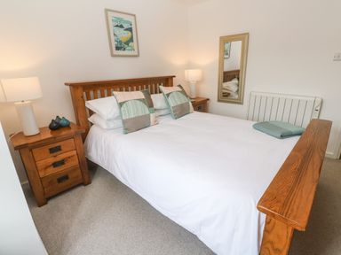 A bedroom with a wooden double bed two bedside tables with lamps a wall mirror and a framed picture at Anneth Lowen Angarrack near Hayle