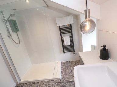 A bathroom with a walk-in shower a black towel rack with towels a sink and a pendant light at Anneth Lowen Angarrack near Hayle