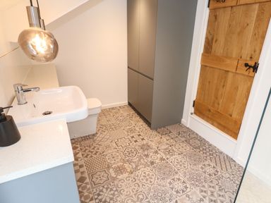 A bathroom with a patterned tiled floor a white sink gray cabinets and a wooden door at Anneth Lowen in Angarrack near Hayle