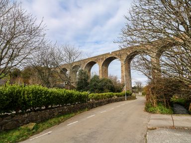 A road with stone wall bushes and bare trees under a stone arch railway viaduct at Anneth Lowen in Angarrack near Hayle