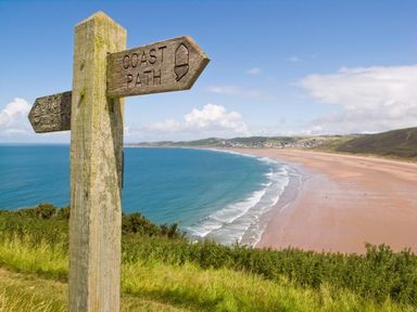 A wooden signpost with coast path arrows overlooking a beach and ocean with hills in the background at Nairn in Braunton