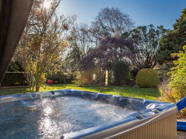 A bubbling hot tub in a garden with trees shrubs and a children's swing set at Nairn in Braunton