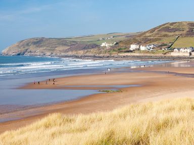 A beach with people walking near the shore hills with houses in the background at Nairn in Braunton