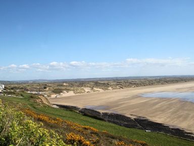 A view of a sandy beach with rocky outcrops green grass and yellow flowers on the hill at Nairn in Braunton