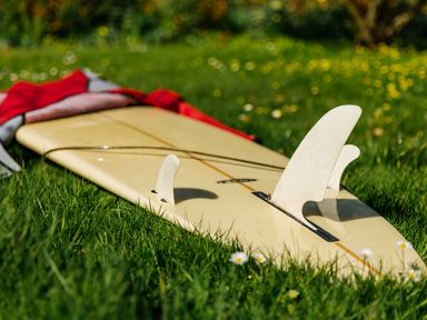 A surfboard with fins lying on grass with a red cloth draped over part of it at Nairn in Braunton