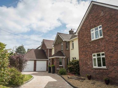 A driveway leading to a two garage doors attached to a brick and cream house with plants in pots at Nairn in Braunton