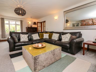 A living room with a dark leather sectional sofa and a square coffee table on a multicolored rug at Nairn in Braunton