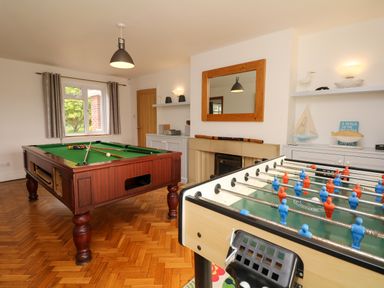 A game room with a pool table, foosball table, fireplace, shelves with decorations, and a window at Nairn in Braunton
