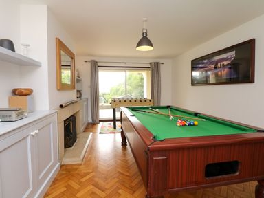 A game room with a pool table and foosball table next to a fireplace and sliding glass doors at Nairn in Braunton