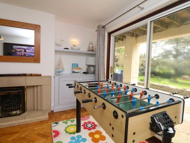 A room with a foosball table on a floral rug near a fireplace and a sliding glass door showing a garden at Nairn in Braunton