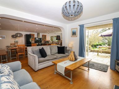 An open-plan living and dining area with sofas a wooden coffee table a dining table and chairs and a kitchen in the background with outdoor view at Nairn in Braunton