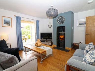 A living room with two sofas a wooden coffee table a wood stove and an open door leading outside at Nairn in Braunton