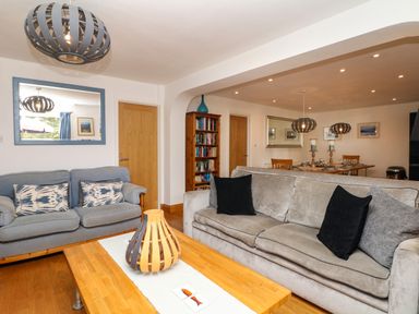 A living room with two sofas a wooden coffee table a bookshelf and a dining area at Nairn in Braunton