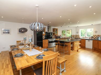 A dining table set with plates and glasses next to a kitchen with an island and appliances at Nairn in Braunton