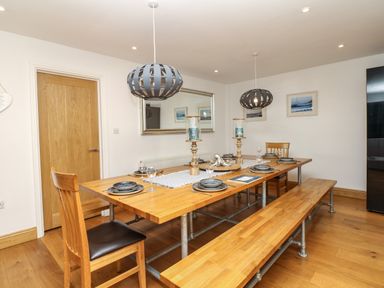 A dining room with a wooden table set with plates and glasses and wooden chairs and benches at Nairn in Braunton