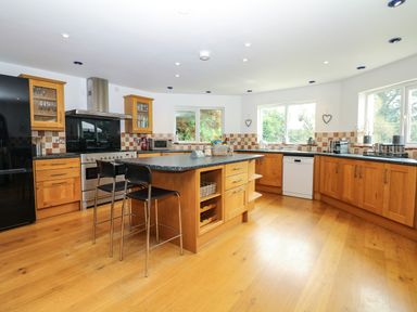 A kitchen with wooden cabinets a central island with chairs and large windows at Nairn in Braunton