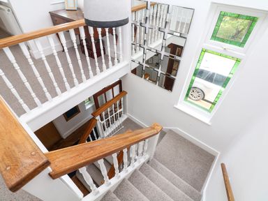 A staircase with a wooden handrail and white balusters beside a window with green stained glass at Nairn in Braunton