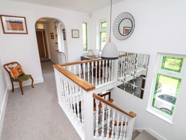 A hallway with a wooden chair and a staircase with white balusters and wooden handrails at Nairn in Braunton