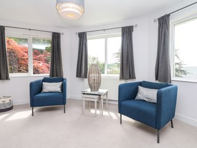 A sitting room with two blue armchairs a small table and three windows at Nairn in Braunton