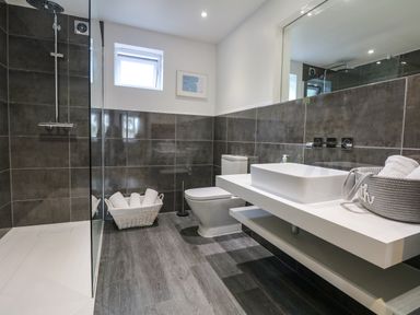 A bathroom with a shower area a toilet a sink with a countertop and baskets with towels at Nairn in Braunton