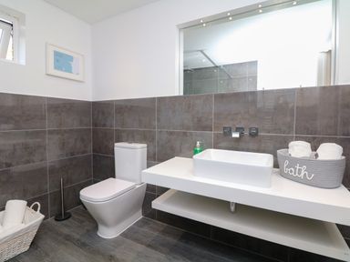 A bathroom with a toilet a sink with a soap dispenser and baskets with towels at Nairn in Braunton