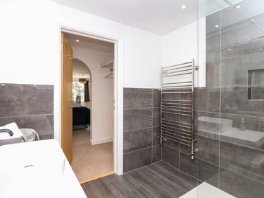 A bathroom with a heated towel rail and walk-in shower next to a doorway leading to a bedroom at Nairn in Braunton