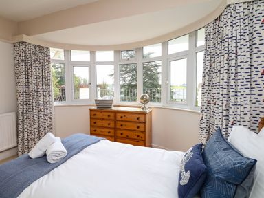 A bedroom with a bed and blue pillows by windows with patterned curtains at Nairn in Braunton