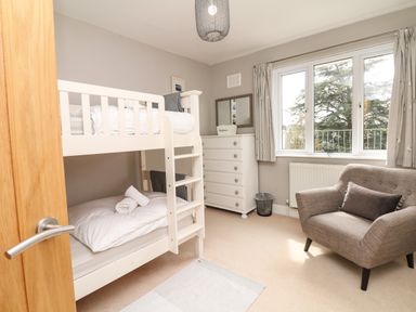 A bedroom with bunk beds a dresser a chair and a window with curtains at Nairn in Braunton