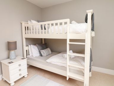 A bedroom with a white bunk bed a bedside table with a lamp and cushions on the beds at Nairn in Braunton