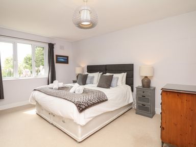 A bedroom with a double bed pillows bedside tables lamps a window with curtains and a wooden dresser at Nairn in Braunton