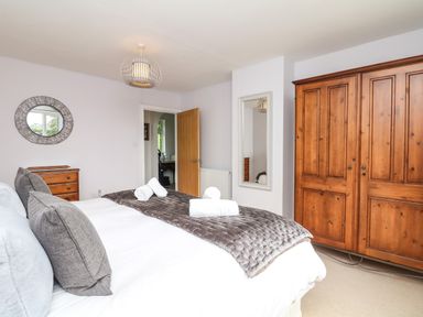 A bedroom with a large bed pillows and folded towels a wooden wardrobe a chest of drawers a round wall mirror and a wall mirror at Nairn in Braunton
