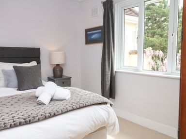 A bedroom with a bed with pillows and rolled towels a bedside table with a lamp and a window with curtains at Nairn in Braunton