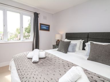 A bedroom with a made bed with pillows and rolled towels near a window with dark curtains at Nairn in Braunton