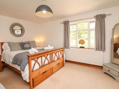 A bedroom with a wooden bed with gray pillows and folded towels and a window with curtains at Nairn in Braunton