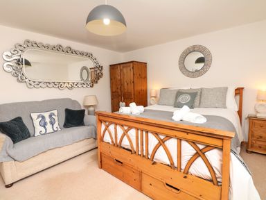 A bedroom with a wooden bed and grey pillows next to a sofa with seahorse cushions at Nairn in Braunton