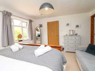 A bedroom with a bed covered in a gray quilt and white towels on it a dresser with a jug on top and a sofa with a cushion at Nairn in Braunton